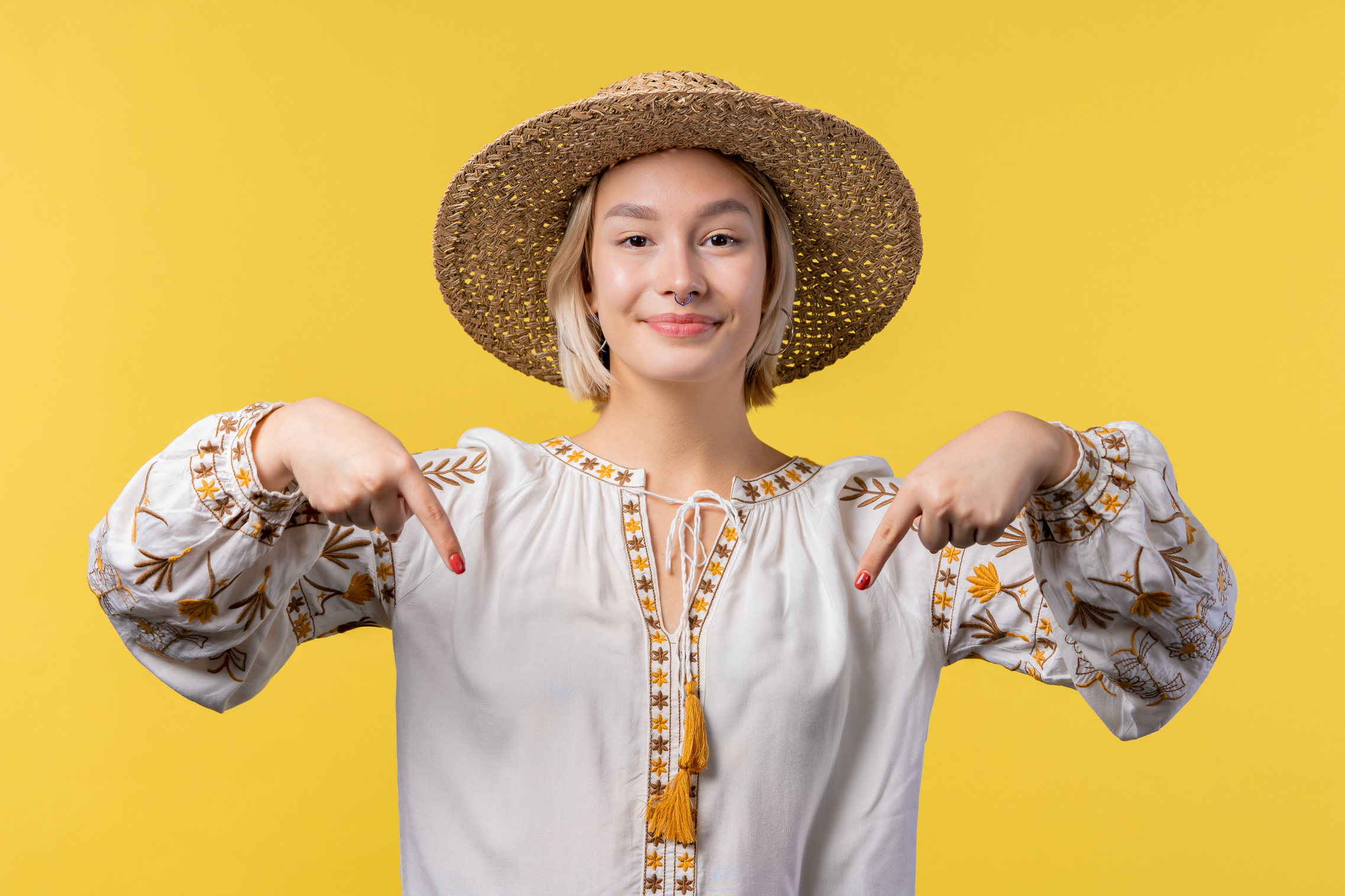 Ukrainian woman pointing down to advertising area. Yellow background. Young lady asking to click to subscribe below. Copy space for your commercial idea, promotional content.